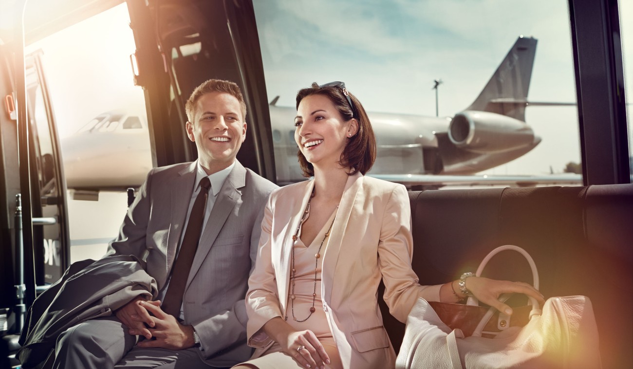 : Geschäftsleute sitzen im Wartebereich am Flughafen und lächeln vor einem Flugzeug.