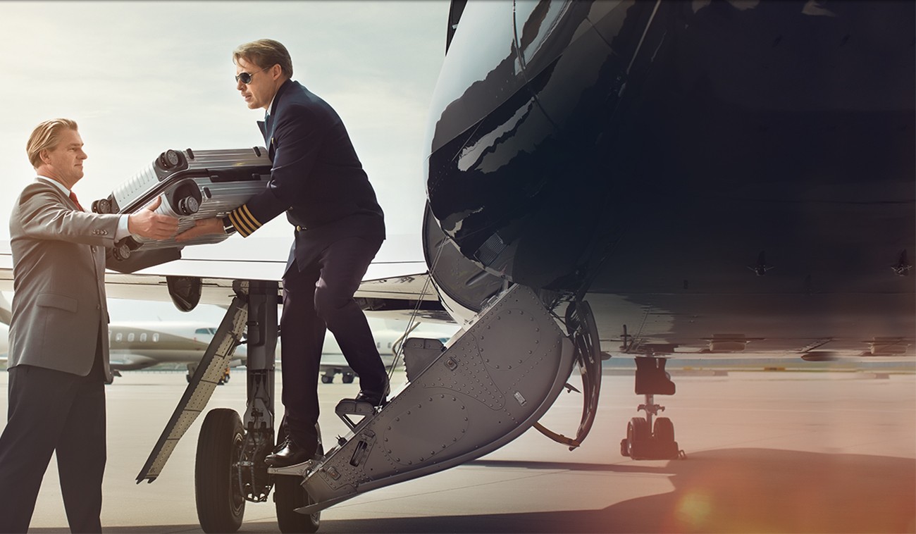 : Ein Mann übergibt am Flugzeug sein Gepäck an einen Mitarbeiter.